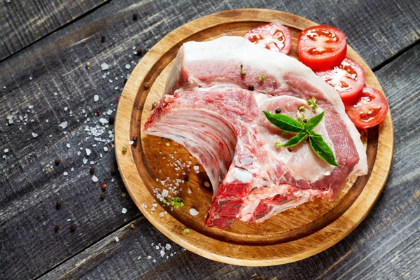 Carne cruda costillas filete de hueso, cerdo con albahaca y tomates en un corte —  Fotos de Stock