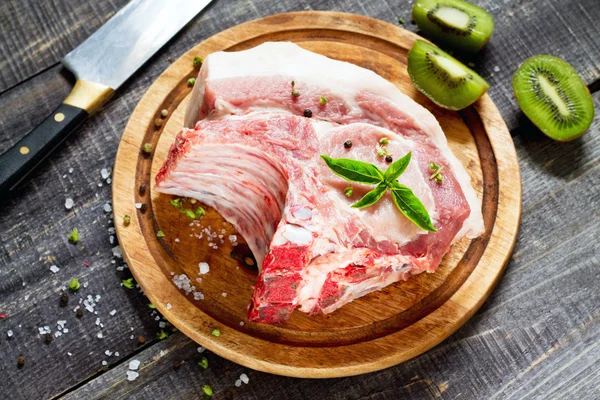 Carne cruda costillas filete de hueso, cerdo con albahaca y kiwi fruta en un cu —  Fotos de Stock