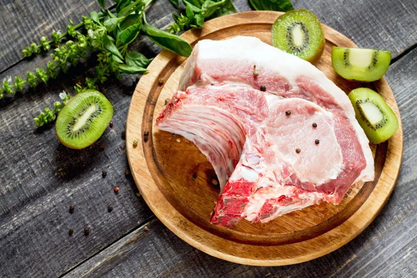 Carne cruda costillas filete de hueso, cerdo con albahaca y kiwi fruta en un cu —  Fotos de Stock