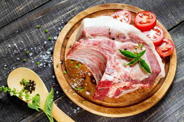 Carne cruda costillas filete de hueso, cerdo con albahaca y tomates —  Fotos de Stock