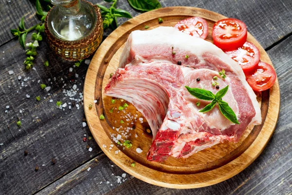 Costillas de carne cruda filete de hueso, cerdo con albahaca, aceite y tomates —  Fotos de Stock