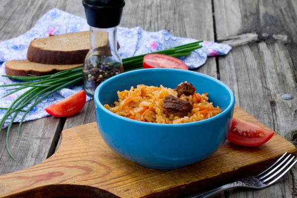 Pilaf con carne y tomates sobre fondo de madera — Foto de Stock