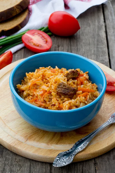 Pilaf con carne y tomates sobre fondo de madera — Foto de Stock