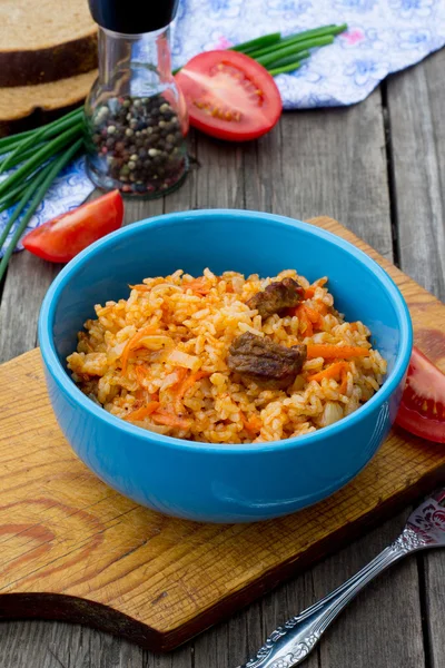 Pilaf con carne y tomates sobre fondo de madera — Foto de Stock