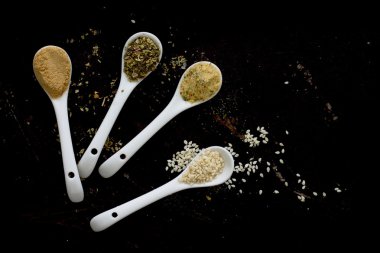 Baharat karanlık bir arka plan üzerinde kaşıklarla (tuz, zencefil, susam, ben