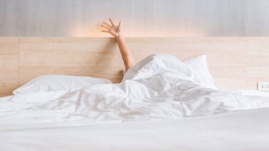 Man waking up and stretching his arm on the bed in white blanket at morning time
