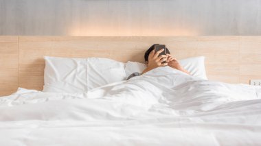 Man waking up and use smartphone or mobile phone on the bed in white blanket at morning time, social lifestyle concept