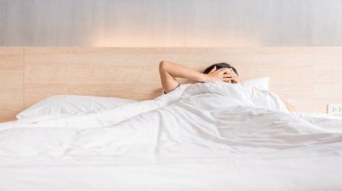 Man waking up and stretching his arm on the bed in white blanket at morning time, laziness concept