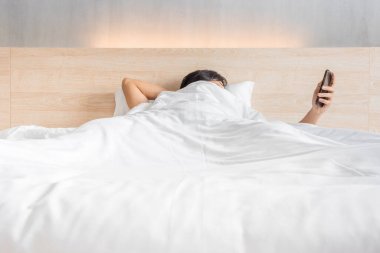 Man waking up and use smartphone or mobile phone on the bed in white blanket at morning time, social lifestyle concept