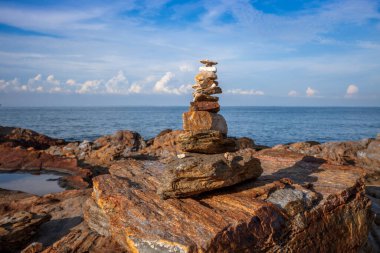 Zen rock stack or cairn balanced on the rugged coastal rocks at Khao Laem Ya National Park, Rayong, Thailand, with the blue ocean and sky in the background