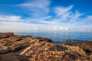 Striking coastal rock formations at Khao Laem Ya National Park, Rayong, Thailand, contrasting with the calm blue ocean and wispy clouds under a bright summer sky