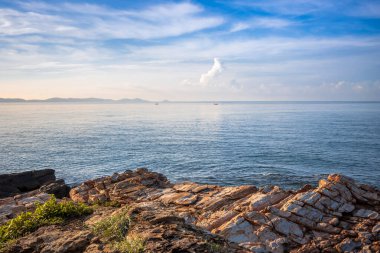 Striking coastal rock formations at Khao Laem Ya National Park, Rayong, Thailand, contrasting with the calm blue ocean and wispy clouds under a bright summer sky