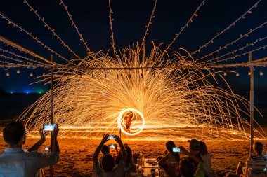 Koh Samet, Rayong, Tayland-2025 Aralık 19: Turistler bir gece etkinliği sırasında plajda olağanüstü bir yangın dönüşü performansı izleyip kaydettiler.
