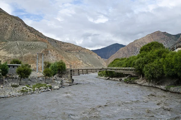 The bridge across affluent mountain Nepal river — Stock Photo, Image