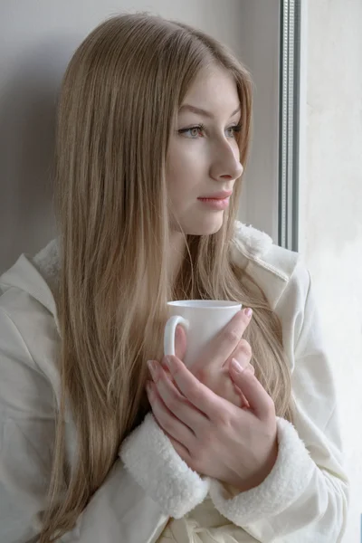 Lovely girl sitting with a hot mug near the window — Stock Photo, Image