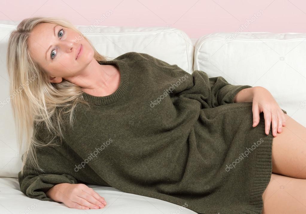 Beautiful tender woman in sweater is posing on a sofa