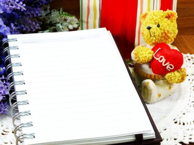 Kağıt arka plan notu ile kırmızı bir kalp ve Noel hediye ile oturan bir oyuncak ayı kitap