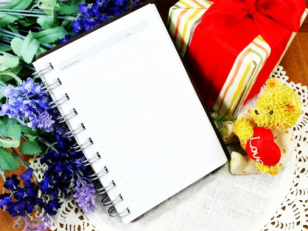 Oso de peluche sentado con un corazón rojo y regalo de Navidad con fondo de papel de libro de notas —  Fotos de Stock