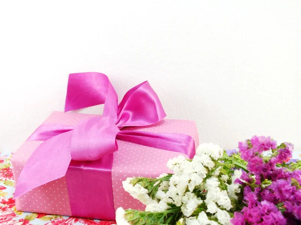 Pink gift box with ribbon and flower bouquet on printed fabric background — Stock Photo, Image