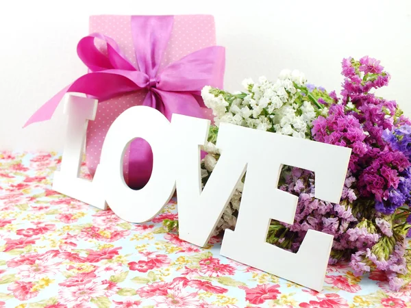 Word love on printed fabric with flower bouquet and craft paper gift box with ribbon bow — Stock Photo, Image