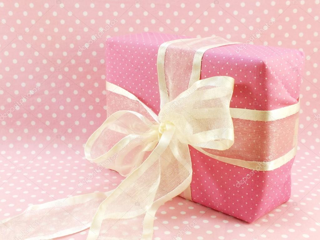 Pink gift box present with white bow on pink polka dot background