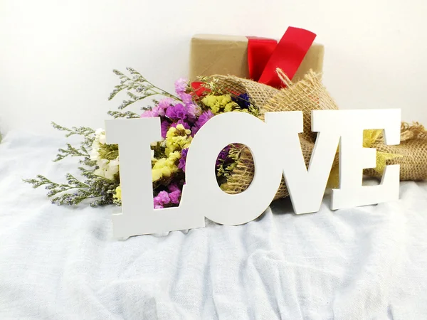 Palavra amor em tecido impresso com buquê de flores e caixa de presente de papel artesanal com laço de fita — Fotografia de Stock