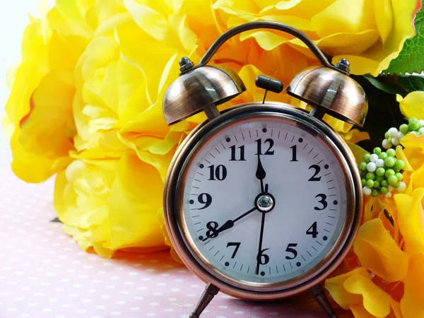 Tavaszi idő ébresztőóra és mesterséges virágok csokor háttér — Stock Fotó
