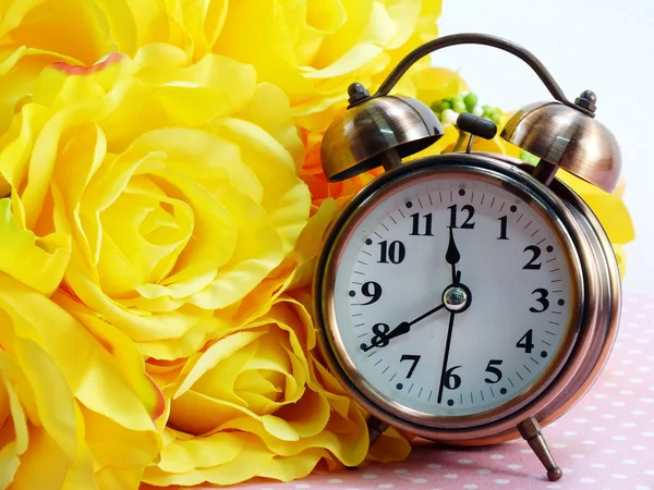 spring time with alarm clock and artificial flowers bouquet background