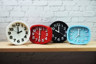 Tahta raflarda ve beyaz tuğlalı arka planda farklı ülkelerin zaman dilimine sahip saatler.