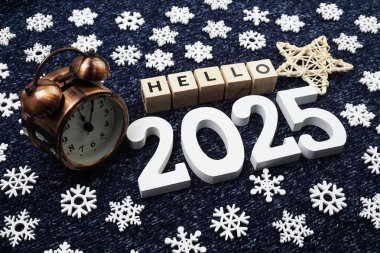 Merhaba 2025 alfabe harfi. Mavi örgü kumaş arka planda alarm saatiyle dekore edilmiş.