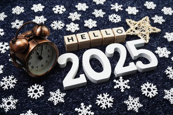 Merhaba 2025 alfabe harfi. Mavi örgü kumaş arka planda alarm saatiyle dekore edilmiş.