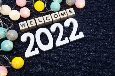 Hoş geldiniz. Mavi örülmüş kumaş zemin üzerinde LED pamuk topu olan 2022 alfabe harfi.