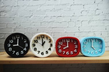 Tahta raflarda ve beyaz tuğlalı arka planda farklı ülkelerin zaman dilimine sahip saatler.