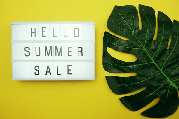 Hello Summer Sale text in light box with green leave on yellow background