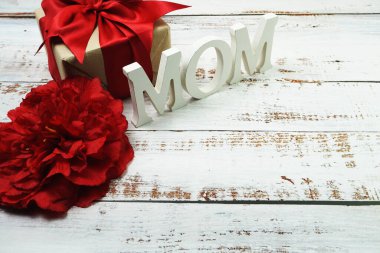 Kırmızı çiçekli anne alfabesi harfi ve tahta arka planda hediye.