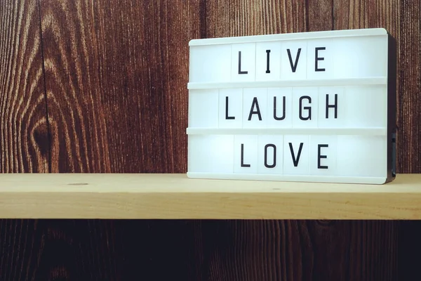 Live Laugh Love word in light box on wooden background