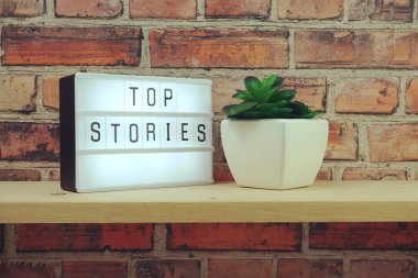 Üst Hikaye kelimesi tuğla duvardaki ışık kutusunda ve ahşap raflarda