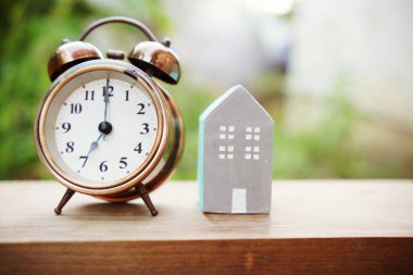 Çalar saat ve ev modeli yeşil arka planlı masada.