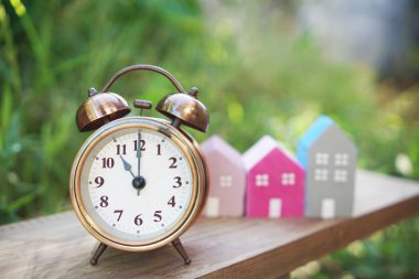 Çalar saat ve ev modeli yeşil arka planlı masada.