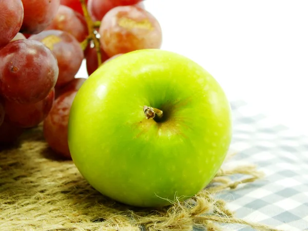 Grüner Apfel und rote Trauben auf Tischdecke — Stockfoto