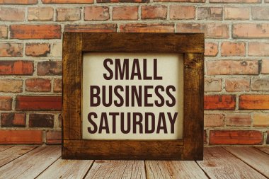 Küçük işletme cumartesi metni tahtaya yazılmış eski tuğla duvar arka planıyla ayakta duruyor