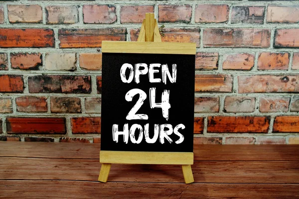 Tahtaya yazılmış 24 saatlik metni aç eski tuğla duvar arkaplanı ile ayakta dur