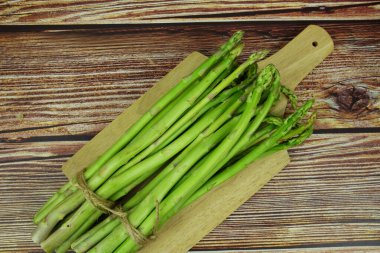 Ahşap arka planda ahşap tahta kesen taze kuşkonmaz sürüsü