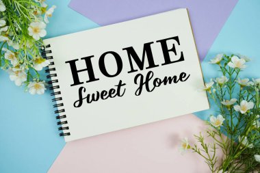 Home Sweet Home metni çiçek süslemeleri ile not defterine yazılmış çok renkli pastel arka planda yatıyordu