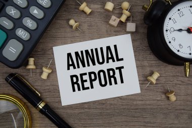 Not defterine kalem, alarm saati, büyüteç ve ahşap zemin üzerinde hesap makinesi ile yazılmış yıllık rapor metni