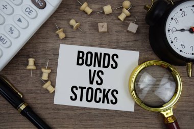 Tahta zemin üzerinde kalem, alarm saati, büyüteç ve hesap makinesi ile not defterine yazılan hisse senetlerine karşı senetler