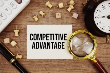 Not defterine kalem, alarm saati, büyüteç ve ahşap zemin üzerinde hesap makinesi ile yazılmış rekabetçi avantaj metni