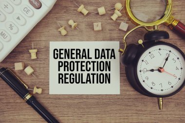 Not defterine kalem, alarm saati, büyüteç ve ahşap zemin üzerinde hesap makinesi ile yazılmış Genel Veri Koruma Düzenleme metni