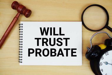 Not defterinde yazan kalem, çalar saat ve ahşap zemin üzerinde yargıç tokmağı olan Will Trust metni