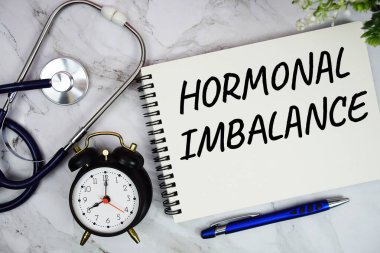 Not defterine steteskop ve mermer zemin üzerinde alarm saati ile yazılmış hormonal dengesizlik metni